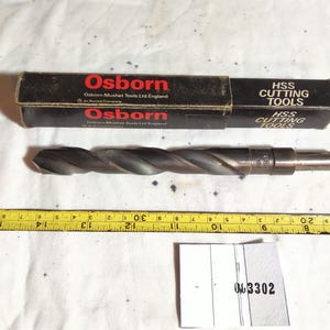 May include: A dark grey HSS twist drill bit positioned above a yellow measuring tape showing a length of approximately 16.5 cm. The drill bit is accompanied by a black rectangular box labelled Osborn HSS CUTTING TOOLS England.