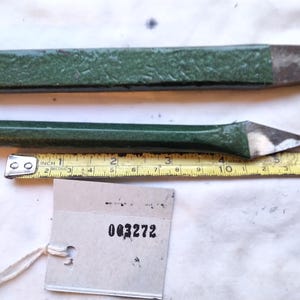 May include: Two green metal chisels with pointed steel tips, positioned above a yellow measuring tape showing a length of approximately 14 cm for the bottom tool. A small grey paper tag with the printed number 003272 is attached below.