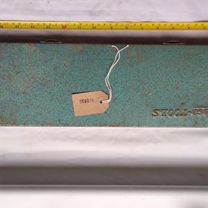 May include: A vintage turquoise metal tool box with the embossed text "Emese-Tools". A yellow measuring tape is placed above the box. A small tag with the number "058030" is attached to the box.