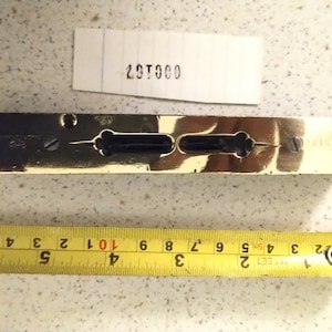 May include: A vintage brass level with a dark center section and two bubble viewing windows. A yellow tape measure shows inches. A piece of paper with the number "29T000" is above the level.