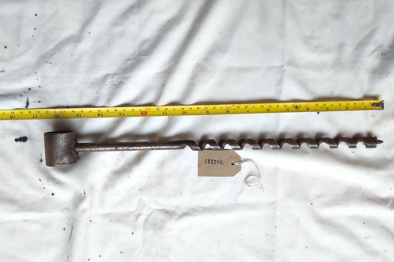 Peut inclure: Une ancienne m&egrave;che de tari&egrave;re avec une poign&eacute;e cylindrique et un bord de coupe en spirale. Un m&egrave;tre ruban jaune indique que la m&egrave;che mesure environ 51 cm de long. Une &eacute;tiquette avec le num&eacute;ro "C82203" est attach&eacute;e.