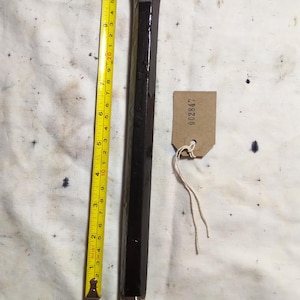 Peut inclure: Un ciseau rectangulaire foncé avec une tête en métal et un manche en bois. Un mètre ruban jaune indique que le ciseau mesure environ 28 cm de long. Une petite étiquette avec le numéro "002847" est attachée.