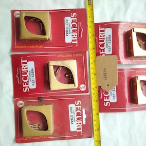 May include: Several gold-colored chest corners on red packaging with the word "SECURIT" and the reference number "S2654". A yellow measuring tape is placed next to the chest corners. The chest corners are approximately 2 inches wide.