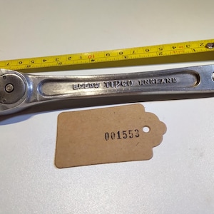 Op de afbeelding: Een zilveren ratelmoersleutel met een zwarte handgreep. De sleutel is gemarkeerd met "Leeds Tipco England".