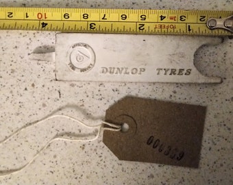 May include: A white plastic tool with the text "DUNLOP TYRES" and a circular logo. A brown paper tag with the number "600000" is attached to the tool with a white string.