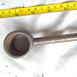 Peut inclure: Gros plan sur un outil en m&eacute;tal rouill&eacute; avec une extr&eacute;mit&eacute; circulaire et une poign&eacute;e cylindrique. Un ruban &agrave; mesurer jaune avec des marques noires est partiellement visible. L'outil semble us&eacute; et vieilli.