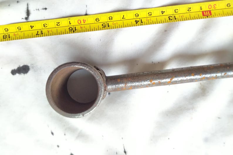 Peut inclure: Gros plan sur un outil en m&eacute;tal rouill&eacute; avec une extr&eacute;mit&eacute; circulaire et une poign&eacute;e cylindrique. Un ruban &agrave; mesurer jaune avec des marques noires est partiellement visible. L'outil semble us&eacute; et vieilli.