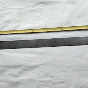 May include: A metal ruler with markings in inches and centimeters. The ruler is 12 inches long and has a yellow tape measure next to it.