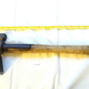 May include: A vintage claw hammer with a wooden handle and a metal head. The hammer is placed on a white surface with a yellow measuring tape in the background. The hammer's head is dark, and the handle is light brown.