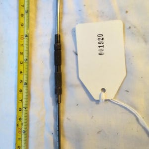 May include: A metal pick tool with a bent tip, approximately 6 inches long, with a textured handle. A white tag with the number 001920 is attached. A yellow measuring tape is in the image.