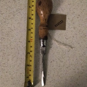 May include: A vintage screwdriver with a wooden handle and a metal blade. The handle is brown and has a worn finish. The blade is silver and has a slight curve at the tip. The screwdriver is about 6 inches long.
