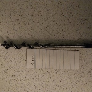 Puede incluir: Una broca de metal plateado con un eje retorcido y un mango plano. La broca está sobre una superficie blanca con un trozo de papel que dice "0519".