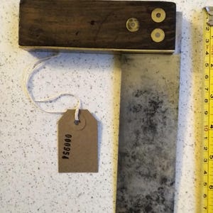 以下が含まれることがあります： 真鍮製のハンドルとリベットが2つ付いた、ヴィンテージの木製と金属製の曲尺。曲尺は、茶色の木製のハンドルと、緑青の付いた金属製の刃を持っています。刃には「000954」という番号が刻印されています。