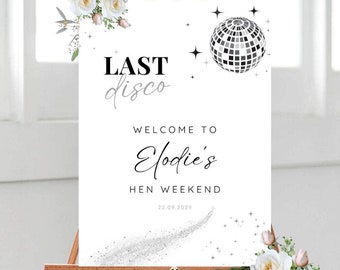 May include: A white welcome sign with black text that reads "Last Disco" and a silver glitter trail. The sign also includes a black and white disco ball graphic and the text "Welcome to Elodie's Hen Weekend 22.09.2023".