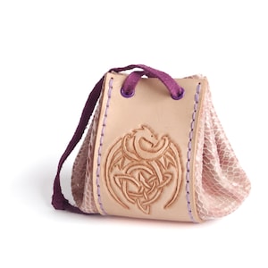 May include: A small, pink leather pouch with a purple drawstring and a leather flap featuring a tooled design of a dragon and a Celtic knot.
