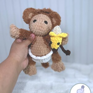 May include: A brown crocheted monkey wearing a white diaper and holding a yellow crocheted banana.