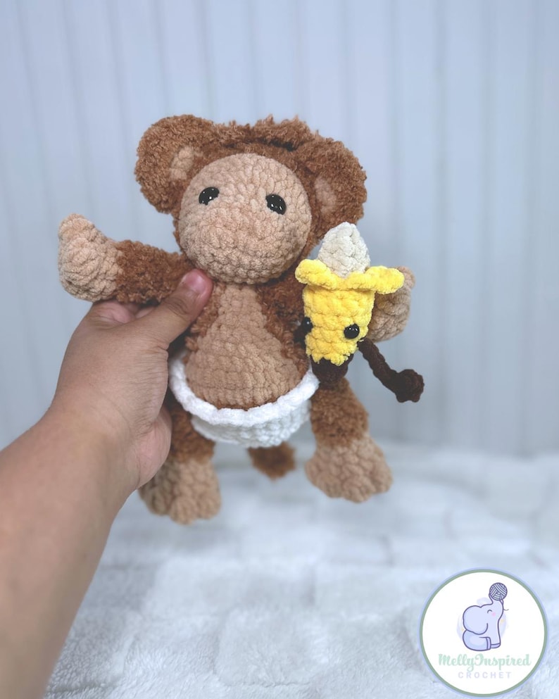 May include: A brown crocheted monkey wearing a white diaper and holding a yellow crocheted banana.