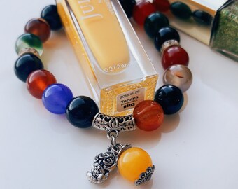 Pode incluir: Um frasco de esmalte de unha amarelo com o nome da marca "Julep" e o texto "Tenaya #103" no rótulo. Uma pulseira de contas multicoloridas com um amuleto de prata pendura no frasco.