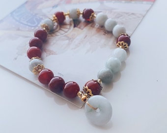 May include: A red and white beaded bracelet with a jade pendant. The bracelet has gold accents and is made of natural stones.