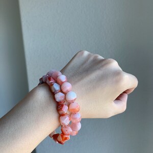 May include: Two bracelets made of pink and orange carnelian beads. The beads are faceted and have a natural, polished look.