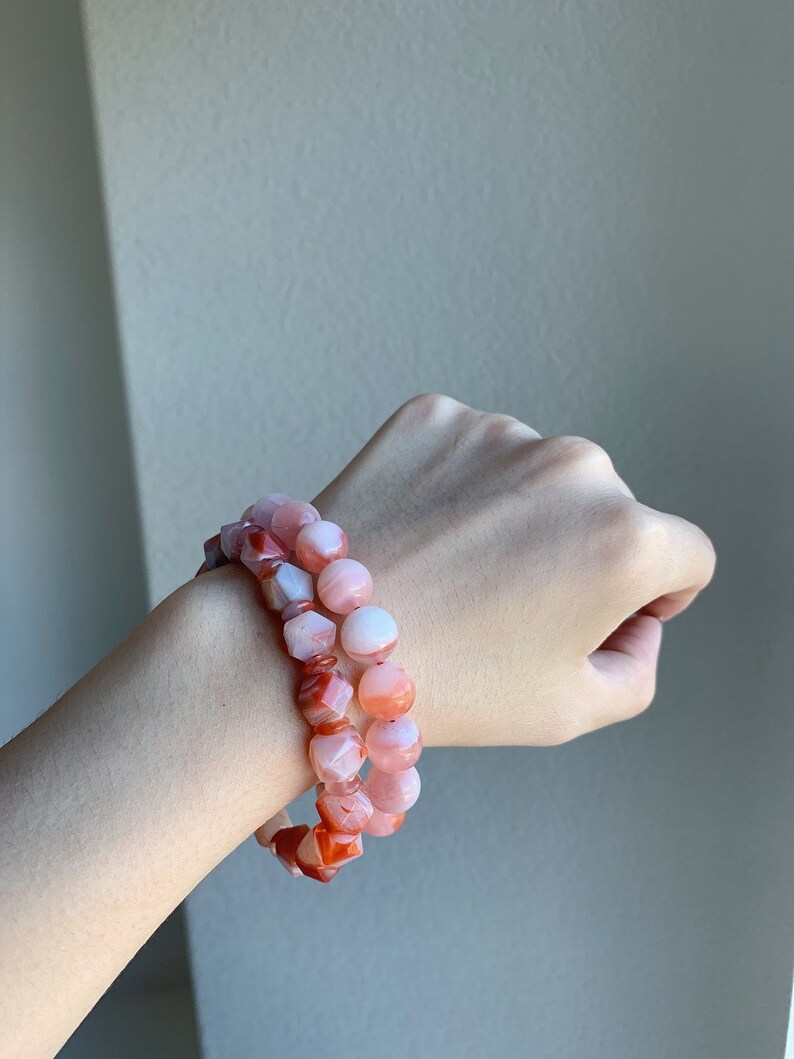 May include: Two bracelets made of pink and orange carnelian beads. The beads are faceted and have a natural, polished look.