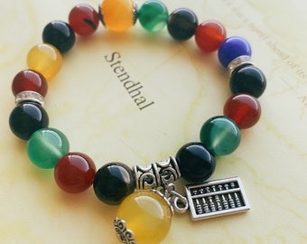 Pode incluir: Um bracelete de contas coloridas com um amuleto de ábaco prateado. O bracelete tem contas verdes, vermelhas, amarelas, pretas e azuis.