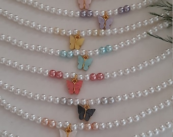 May include: A set of pearl necklaces with colorful butterfly charms. Each necklace features a different color butterfly charm, including green, pink, purple, yellow, blue, red, and white.