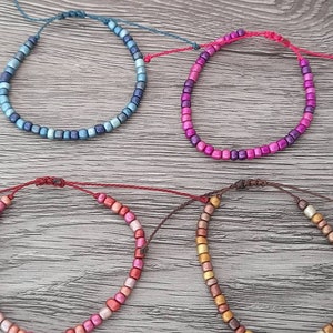 Puede incluir: Cuatro pulseras de cuentas coloridas con diferentes degradados de color. Las pulseras están hechas con cuentas pequeñas y cuadradas y están atadas con un hilo delgado.