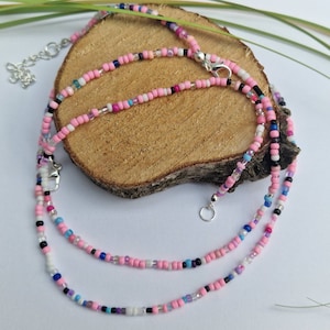 Könnte beinhalten: Eine mehrreihige Halskette mit rosa, weißen, blauen und schwarzen Perlen. Die Halskette besteht aus kleinen, runden Perlen und hat einen silbernen Verschluss.