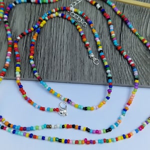 May include: A collection of colorful beaded necklaces. The necklaces feature small, round beads in a variety of colors, including red, yellow, blue, green, and purple. Each necklace has a silver-colored clasp and adjustable chain.