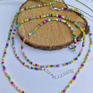 Op de afbeelding: Een veelkleurige kralenketting met een zilveren sluiting. De ketting is gemaakt van kleine, kleurrijke kralen in tinten roze, groen, geel, blauw en paars.