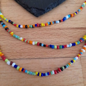 May include: A multi-strand necklace made of colorful glass beads. The beads are in various shades of red, orange, yellow, green, blue, and white. The necklace is layered and has a casual, bohemian style.