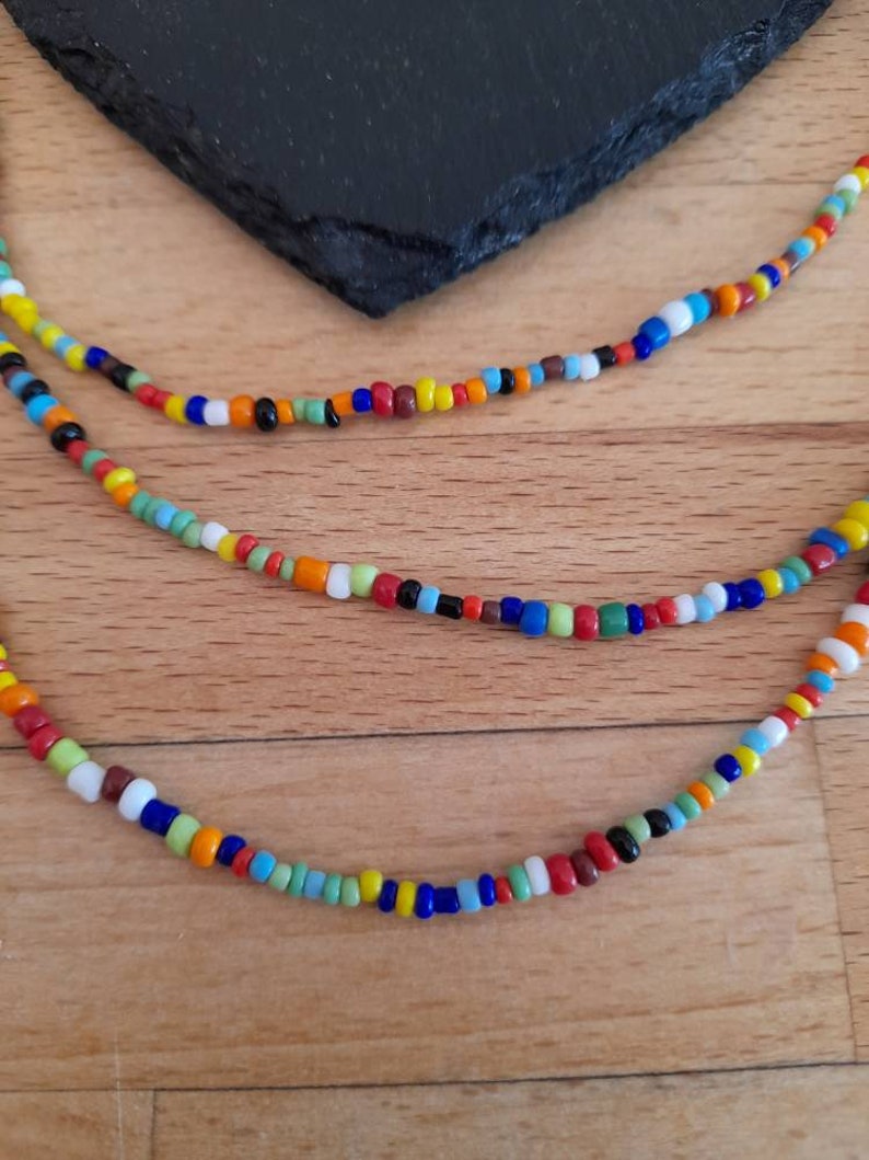 May include: A multi-strand necklace made of colorful glass beads. The beads are in various shades of red, orange, yellow, green, blue, and white. The necklace is layered and has a casual, bohemian style.