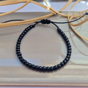 Puede incluir: Un brazalete negro de cuentas con un cierre simple de nudo.