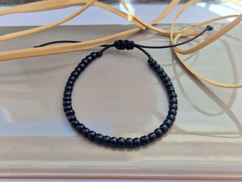Puede incluir: Un brazalete negro de cuentas con un cierre simple de nudo.