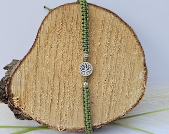 May include: A green braided bracelet with a silver tree of life charm. The bracelet is displayed on a wooden surface.