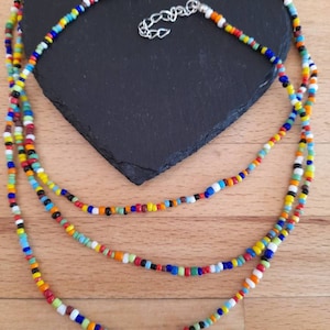May include: A multi-layered necklace made of colorful glass beads. The necklace is made of three strands of beads, each with a different color scheme. The beads are small and round, and they are strung together on a thin cord. The necklace is a vibrant and eye-catching piece of jewelry.