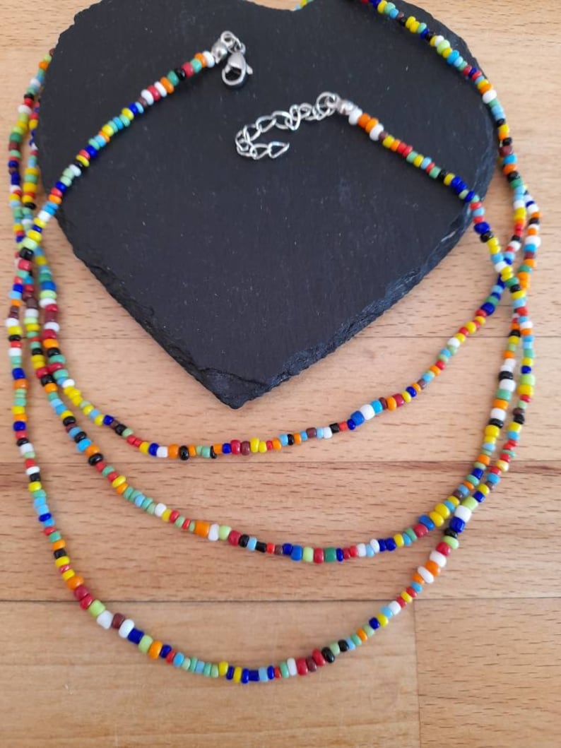 May include: A multi-layered necklace made of colorful glass beads. The necklace is made of three strands of beads, each with a different color scheme. The beads are small and round, and they are strung together on a thin cord. The necklace is a vibrant and eye-catching piece of jewelry.