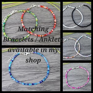 May include: A set of six colorful beaded bracelets or anklets. The bracelets are made with small, colorful beads and have silver clasps. The text "Matching Bracelets / Anklets available in my shop" is written on a wooden background.