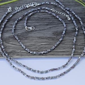 May include: Three silver beaded necklaces with grey and silver beads. The necklaces are layered on a wooden surface.
