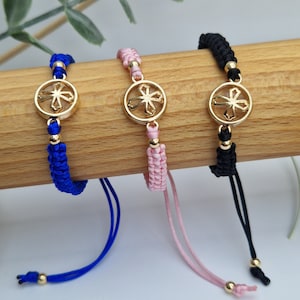 May include: Three braided bracelets with gold charms in the shape of a flower. The bracelets are blue, pink, and black.
