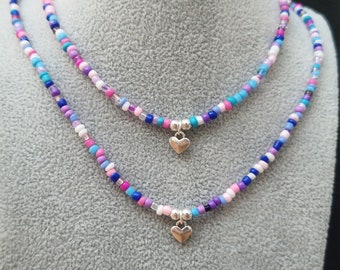 Puede incluir: Dos collares superpuestos con cuentas de colores y colgantes de corazón plateados.