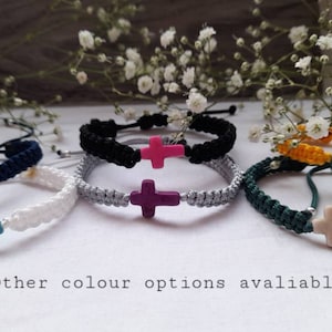 Peut inclure: Six bracelets colorés avec un charme en forme de croix. Les bracelets sont faits de cordon tressé dans différentes couleurs, notamment le blanc, le noir, le gris, le vert, le jaune et le bleu. Chaque bracelet présente un charme en forme de croix de couleur différente.