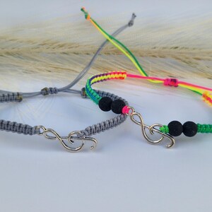May include: Two friendship bracelets with a silver music note charm. One bracelet is grey and the other is multi-coloured with black lava beads.