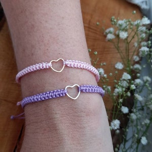 Pode incluir: Duas pulseiras de amizade com pingentes de coração. Uma pulseira é rosa e a outra é roxa.