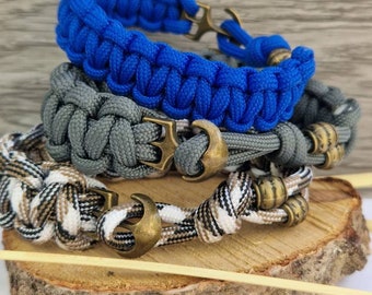 Puede incluir: Tres pulseras trenzadas de paracord con dijes de ancla. Las pulseras son de color azul, gris y camuflaje.