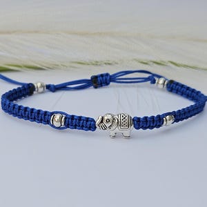 Könnte beinhalten: Ein blaues geflochtenes Armband mit silbernen Perlen und einem silbernen Elefanten-Anhänger.