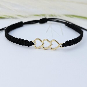 May include: A black braided cord bracelet with a gold charm of three interlocking hearts.
