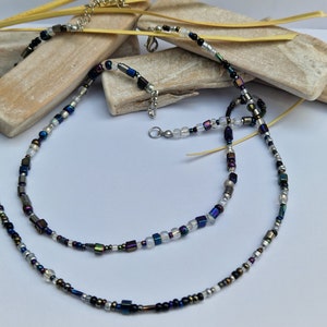 以下が含まれることがあります： 虹色の青、黒、銀のビーズを使った2連ネックレス。ネックレスは、小さな正方形のビーズと丸いビーズで作られています。