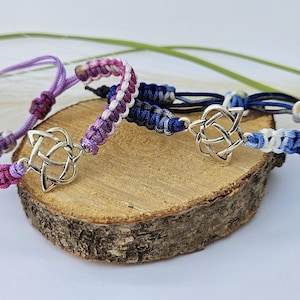 May include: Three braided bracelets with a silver Celtic knot charm. The bracelets are made with purple, blue, and white thread.